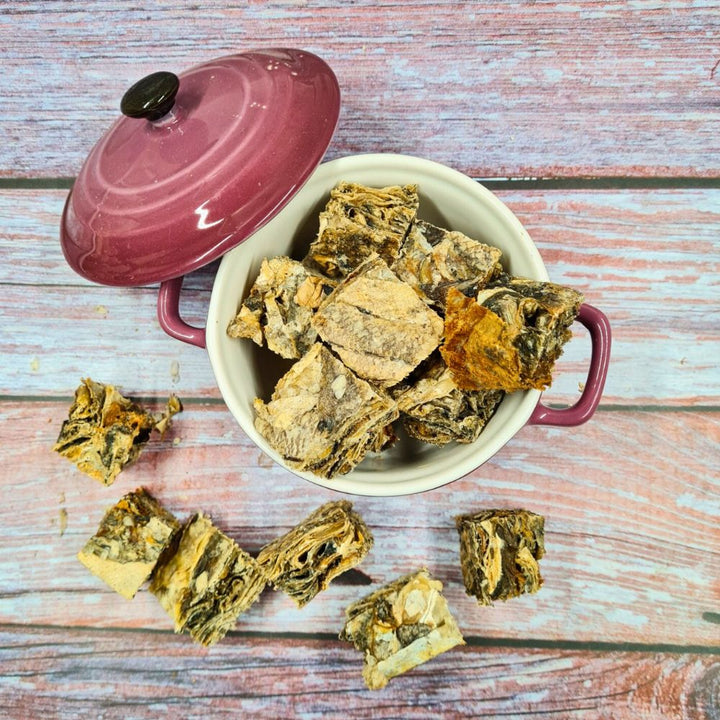 Cubes de morue séchée pour chien, chair et peau, posés sur une planche en bois